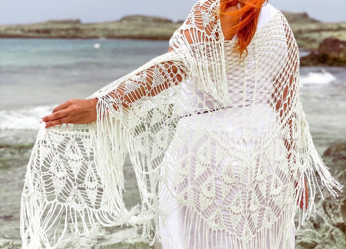 fotografía mía de espaldas mirando al mar, apoyada en la barandilla vestida de blanco y con el chal que diseñé para mi boda.