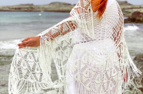 fotografía mía de espaldas mirando al mar, apoyada en la barandilla vestida de blanco y con el chal que diseñé para mi boda.