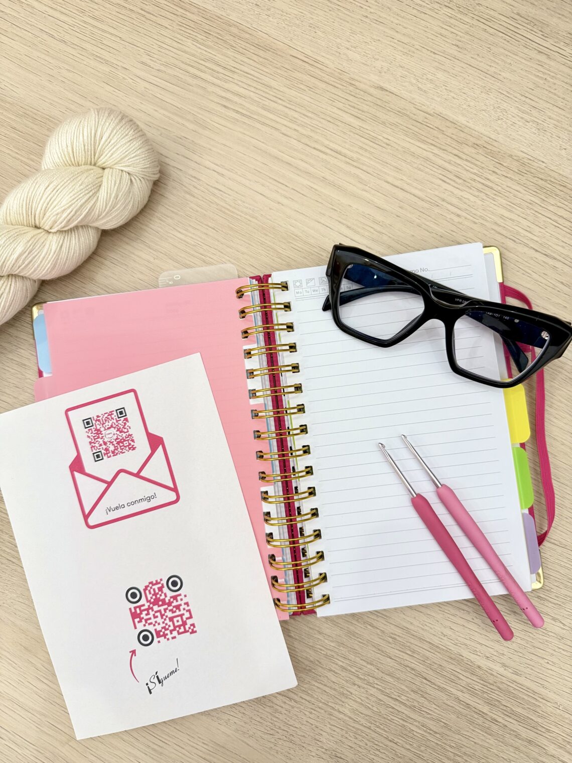 Composición de agenda abierta, códigos QR accesibles, gafas y ganchillossobre mesa de madera clarita