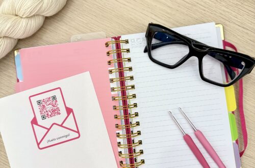 Composición de agenda abierta, códigos QR accesibles, gafas y ganchillossobre mesa de madera clarita